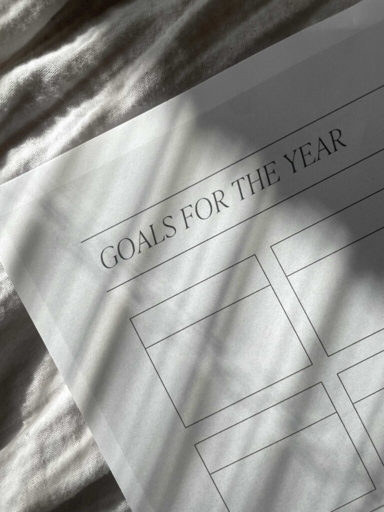 A paper with "Goals for the Year" is laying on a blanket. Shadows from blinds are seen on the paper.