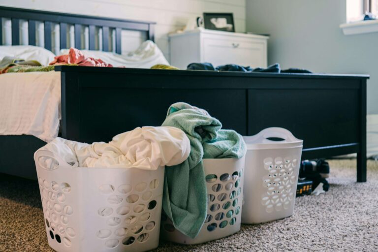 A few overflowing laundry baskets are on the floor at the end of a bed
