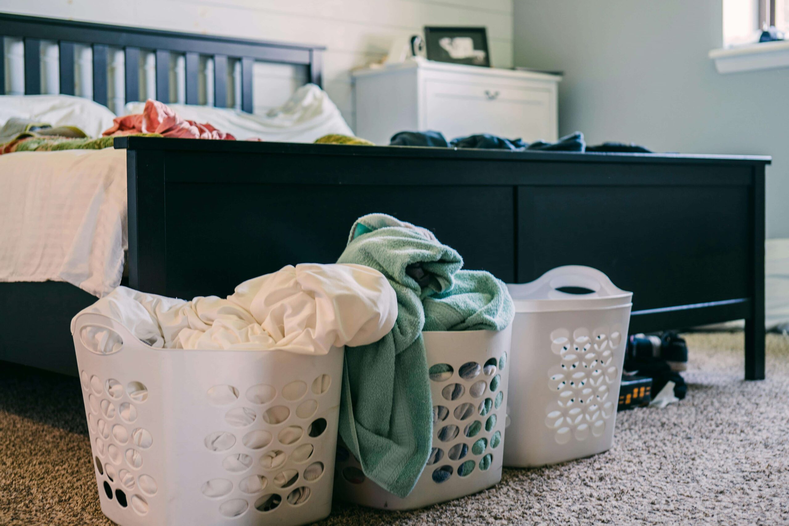 A few overflowing laundry baskets are on the floor at the end of a bed
